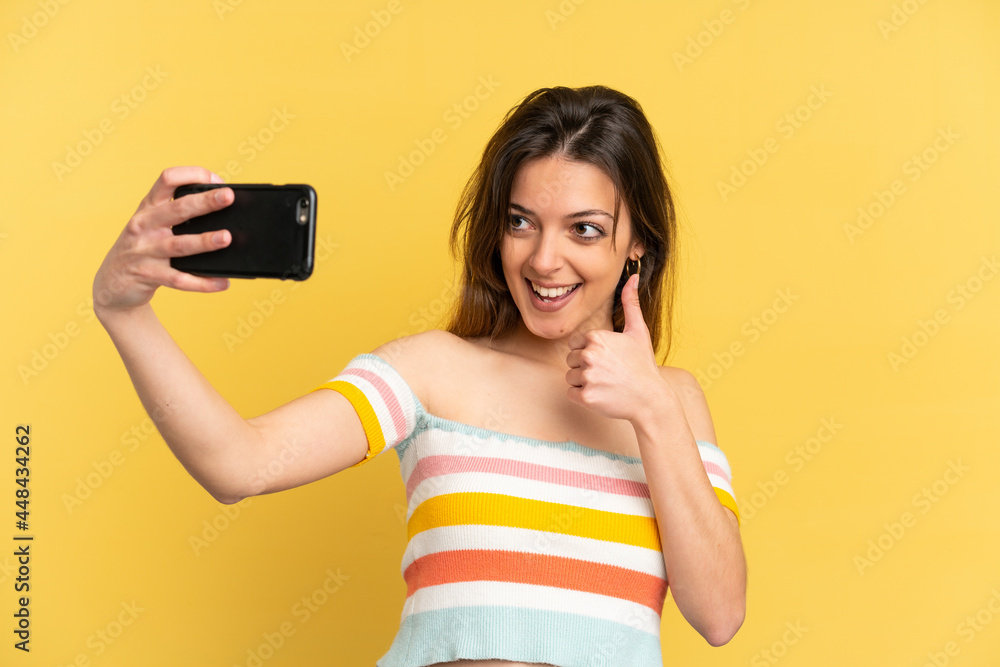 Young caucasian woman isolated on yellow background making a selfie with mobile phone Young caucasian woman isolated on yellow background making a selfie with mobile phone