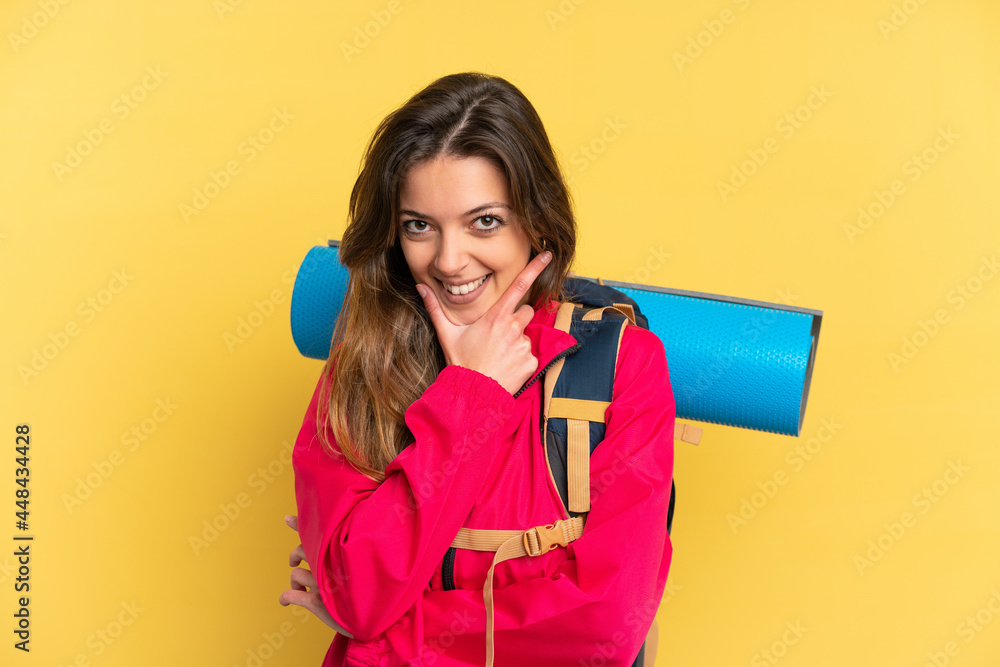 Young mountaineer man with a big backpack isolated on yellow background happy and smiling Young mountaineer man with a big backpack isolated on yellow background happy and smiling