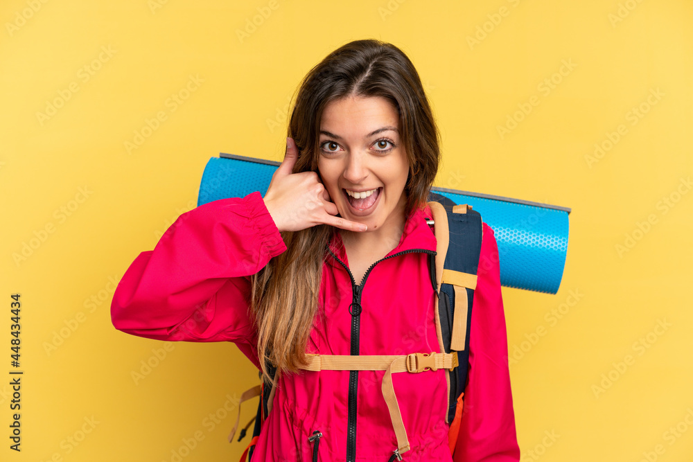 Young mountaineer man with a big backpack isolated on yellow background making phone gesture. Call me back sign Young mountaineer man with a big backpack isolated on yellow background making phone gesture. Call me back sign