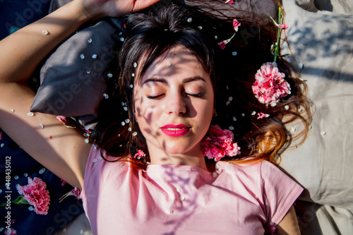 Brunet girl slipping in a bed with flwoer petals, shadows on a face photo