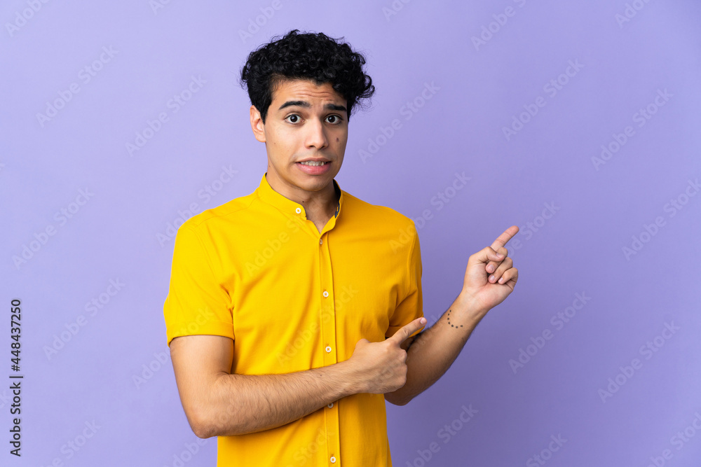 Young Venezuelan man isolated on purple background frightened and pointing to the side Young Venezuelan man isolated on purple background frightened and pointing to the side