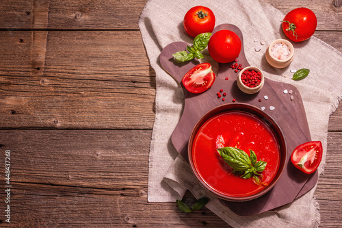 Tomato soup with basil in a bowl. Ripe vegetables, fresh greens, fragrant spices. Vintage wooden table, top view