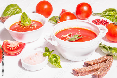 Bowls with homemade tomato soup. Ripe vegetables, fresh basil leaves, breadsticks, aromatic spices