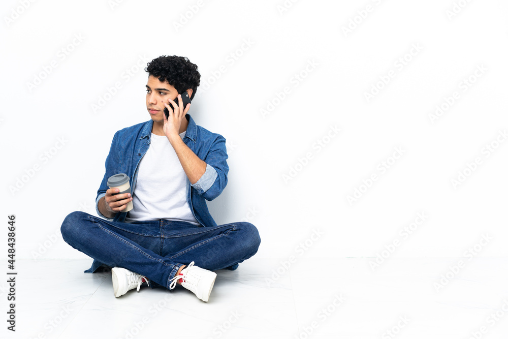 Venezuelan man sitting on the floor holding coffee to take away and a mobile Venezuelan man sitting on the floor holding coffee to take away and a mobile