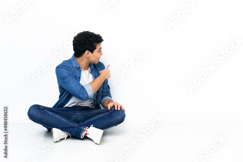 Venezuelan man sitting on the floor pointing back with the index finger © luismolinero