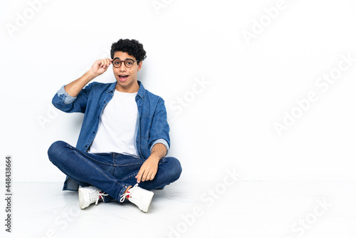 Venezuelan man sitting on the floor with glasses and surprised © luismolinero