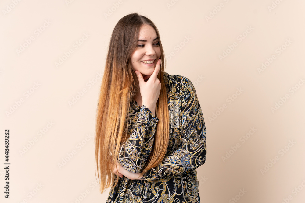 Young caucasian woman isolated on beige background looking to the side and smiling