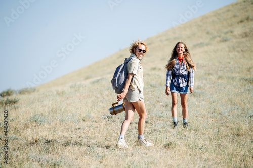Elated best girl friends going uphill, hiking in the grassy hills. Posing