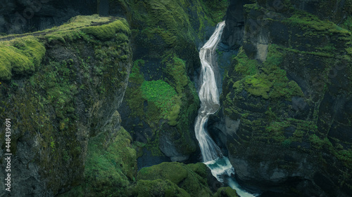 Epic aerial view of Fjaðrárgljúfur Canyon waterfall in southern Iceland. A green lush canyon with steep rocks carved into picturesque landscape in moody hazy atmosphere.