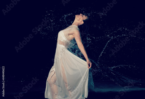 beautiful woman of Caucasian appearance with black hair dances in drops of water on a black background © nndanko