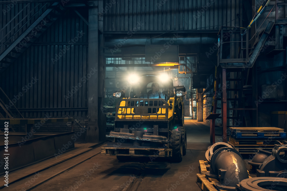 Fototapeta premium Small yellow loading tractor or mower at work in metallurgical factory workshop.