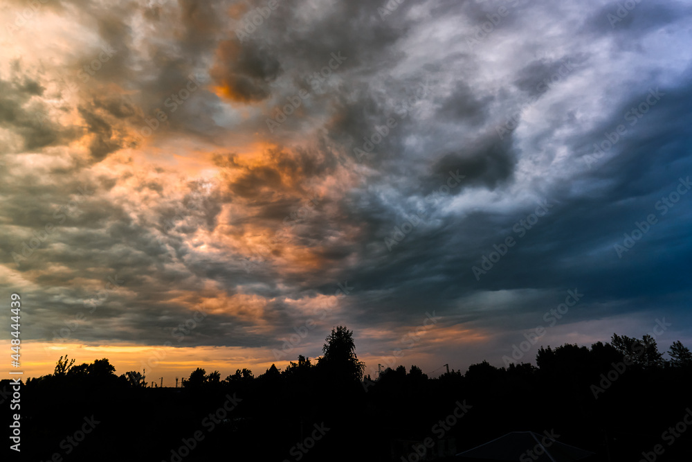 Beautiful natural evening landscape panorama. Silhouette roofs of houses and trees. Hembic clouds at sunset, bright colorful colors of nature