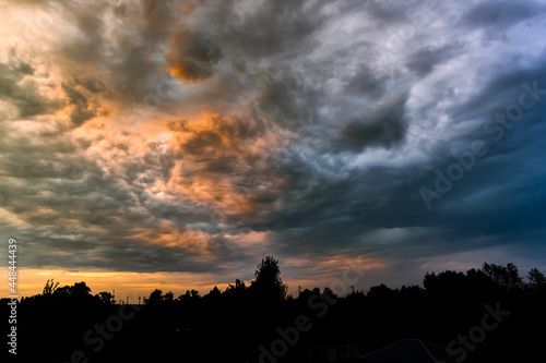 Beautiful natural evening landscape panorama. Silhouette roofs of houses and trees. Hembic clouds at sunset, bright colorful colors of nature