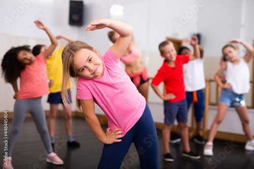 Little girl warming up in group dance class, doing stretching exercises before dance training