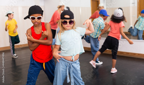 Preteen girl and boy in caps and sunglasses performing hip-hop at group dance class