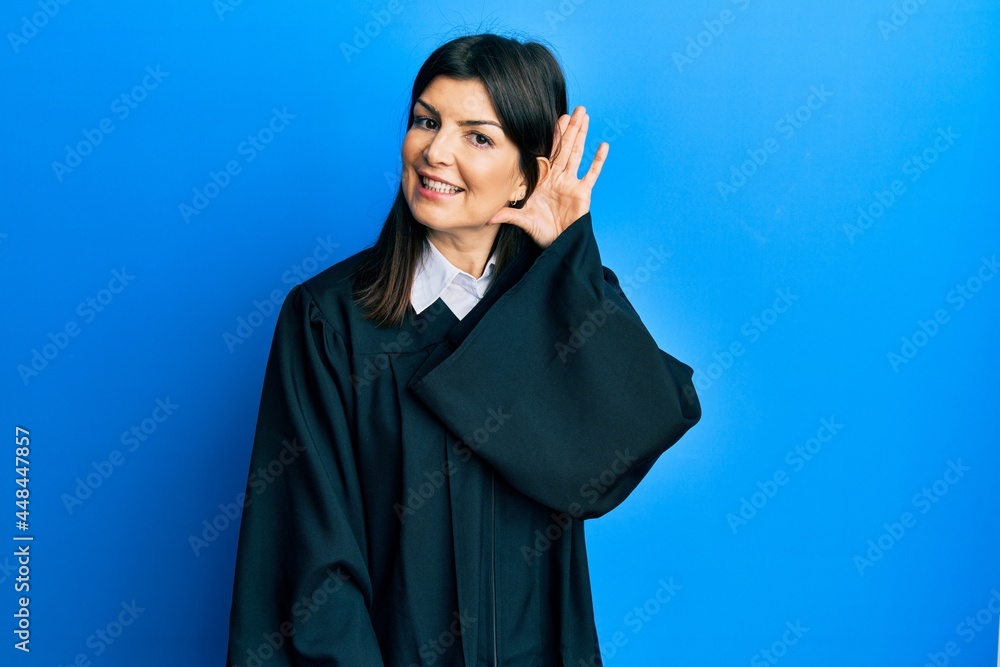 Young hispanic woman wearing judge uniform smiling with hand over ear listening an hearing to rumor or gossip. deafness concept. Young hispanic woman wearing judge uniform smiling with hand over ear listening an hearing to rumor or gossip. deafness concept.