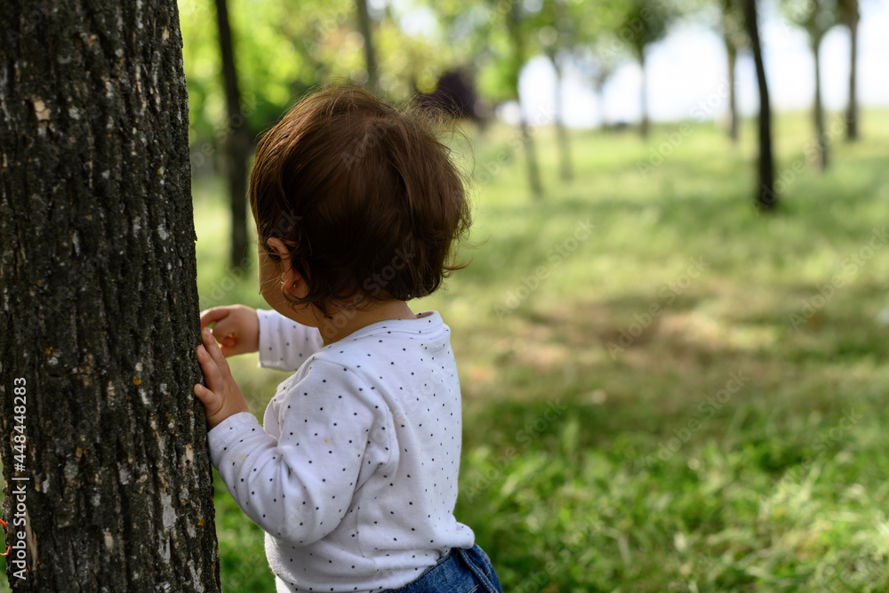 Little girl with her back to the trunk of a tree. Trees background with copy space Little girl with her back to the trunk of a tree. Trees background with copy space