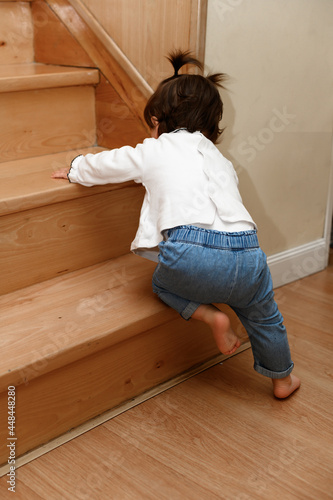 Barefoot toddler tries to climb wooden stairs on all fours