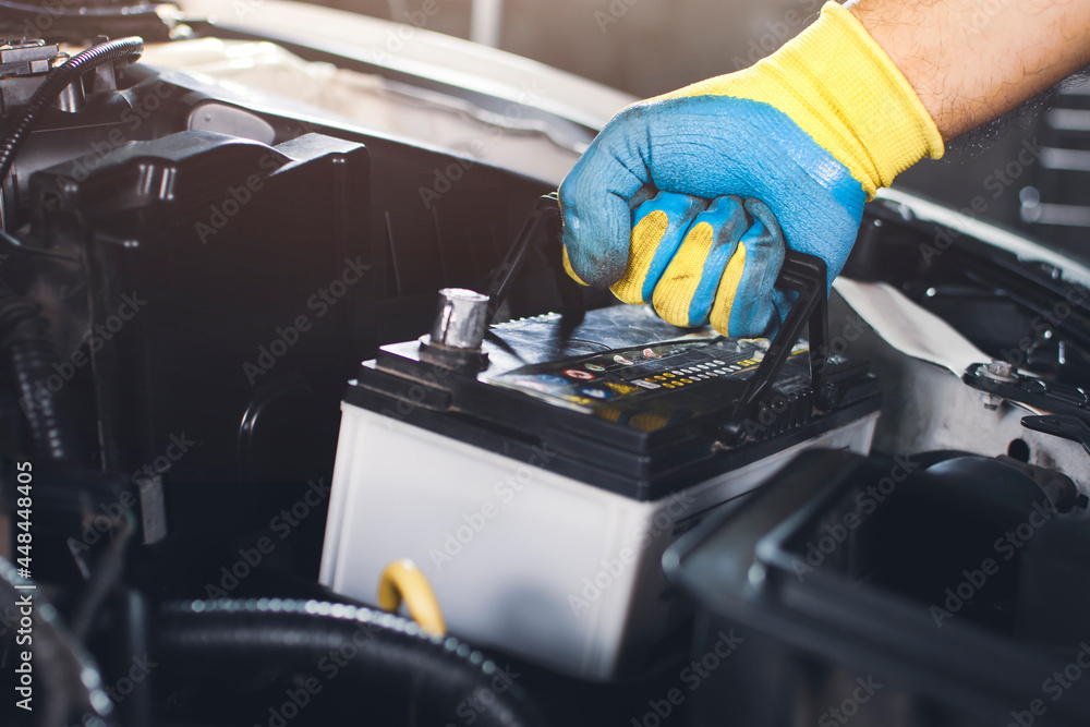 Technician is pulling up an car old battery for replacement - obrazy, fototapety, plakaty 
