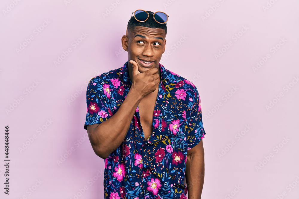 Young black man wearing hawaiian shirt and sunglasses with hand on chin thinking about question, pensive expression. smiling with thoughtful face. doubt concept. Young black man wearing hawaiian shirt and sunglasses with hand on chin thinking about question, pensive expression. smiling with thoughtful face. doubt concept.