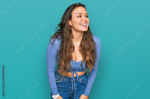 Young hispanic girl wearing casual clothes looking away to side with smile on face, natural expression. laughing confident.