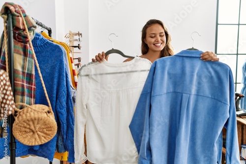 Young hispanic customer woman smiling happy choosing clothes at clothing store.