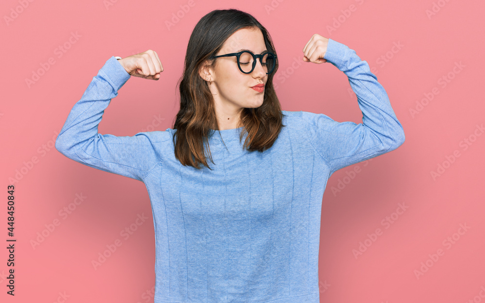 Young beautiful woman wearing casual clothes and glasses showing arms muscles smiling proud. fitness concept.