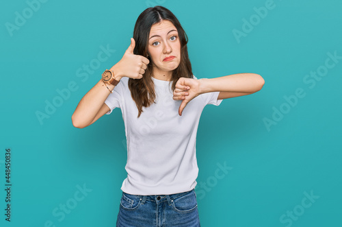 Young beautiful woman wearing casual white t shirt doing thumbs up and down, disagreement and agreement expression. crazy conflict