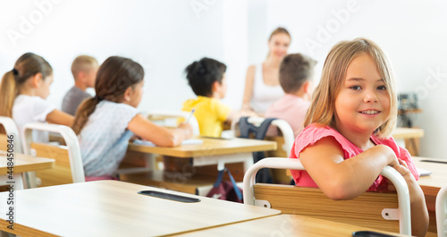 Young girl sitting at desk in class room. She have turned around and looking in camera.