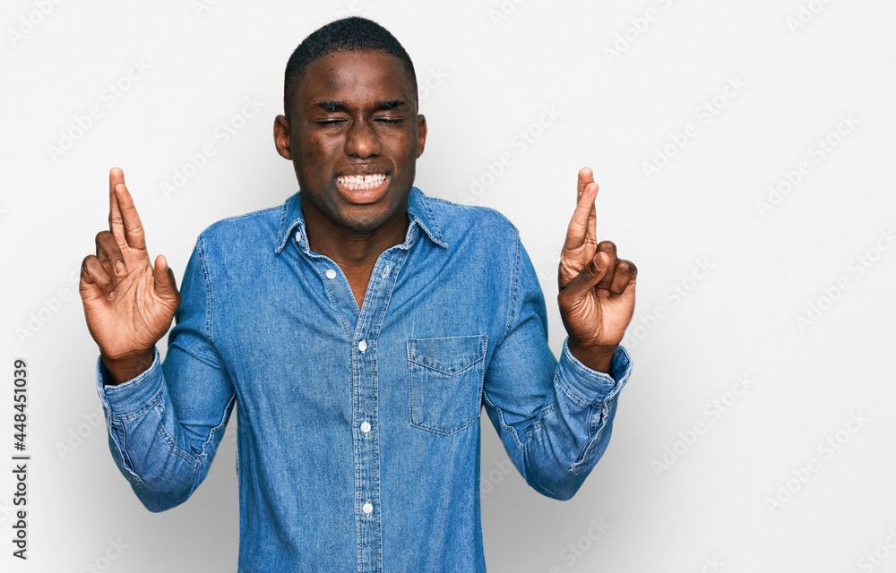Young african american man wearing casual clothes gesturing finger crossed smiling with hope and eyes closed. luck and superstitious concept. Young african american man wearing casual clothes gesturing finger crossed smiling with hope and eyes closed. luck and superstitious concept.