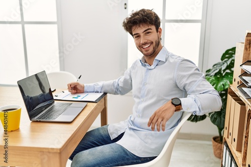 Young hispanic businessman smiling happy working at the office.