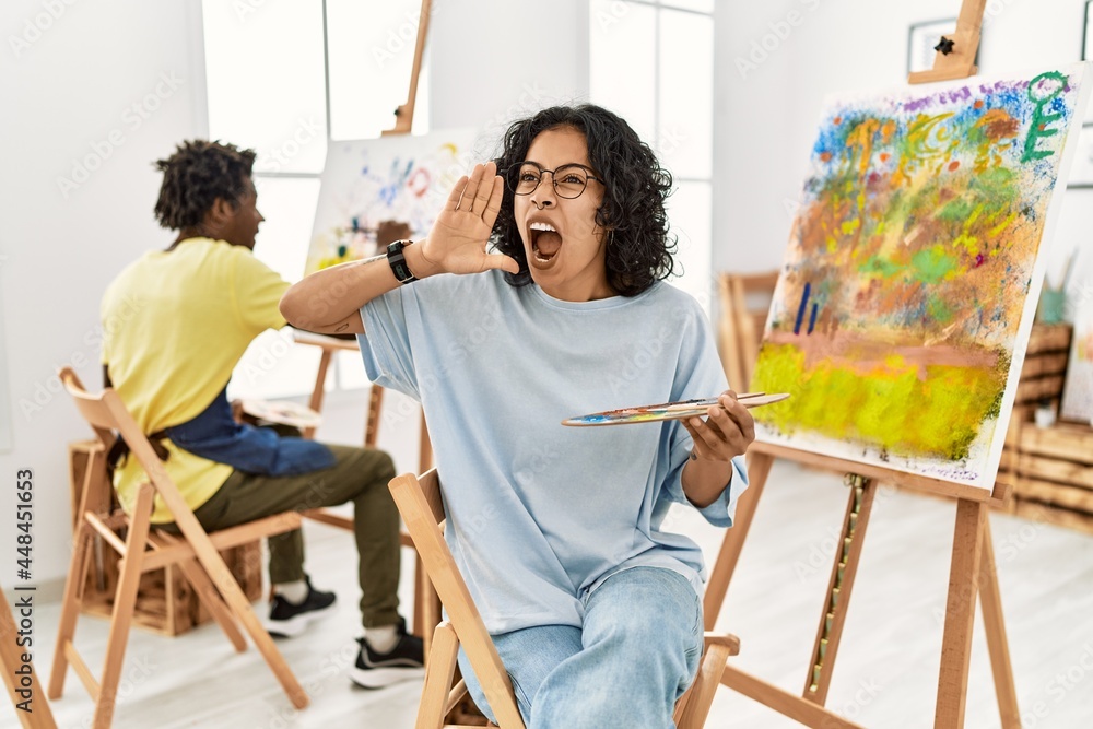 Young hispanic woman at art studio shouting and screaming loud to side with hand on mouth. communication concept. Young hispanic woman at art studio shouting and screaming loud to side with hand on mouth. communication concept.