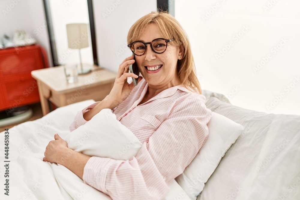 Middle age blonde woman talking on the smartphone lying on the bed at home. Middle age blonde woman talking on the smartphone lying on the bed at home.