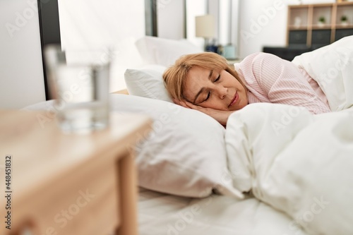 Middle age blonde woman sleeping on the bed at home.