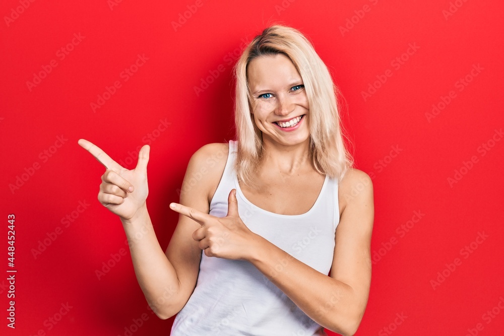 Beautiful caucasian blonde woman wearing casual white t shirt smiling and looking at the camera pointing with two hands and fingers to the side. Beautiful caucasian blonde woman wearing casual white t shirt smiling and looking at the camera pointing with two hands and fingers to the side.