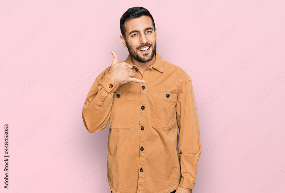 Young hispanic man wearing casual clothes smiling doing phone gesture with hand and fingers like talking on the telephone. communicating concepts. Young hispanic man wearing casual clothes smiling doing phone gesture with hand and fingers like talking on the telephone. communicating concepts.