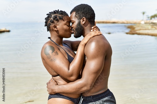 Young african american tourist couple wearing swimwear hugging and kissing at the beach.