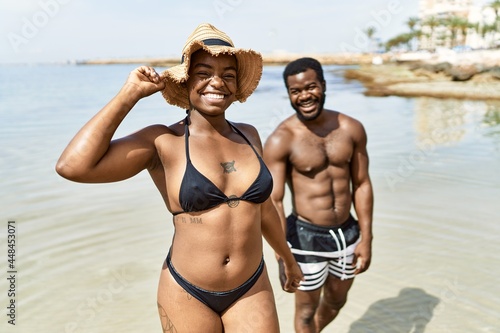 Young african american tourist couple wearing swimwear walking with hands together at the beach.