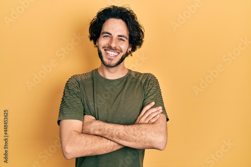 Handsome hispanic man wearing casual green t shirt happy face smiling with crossed arms looking at the camera. positive person.