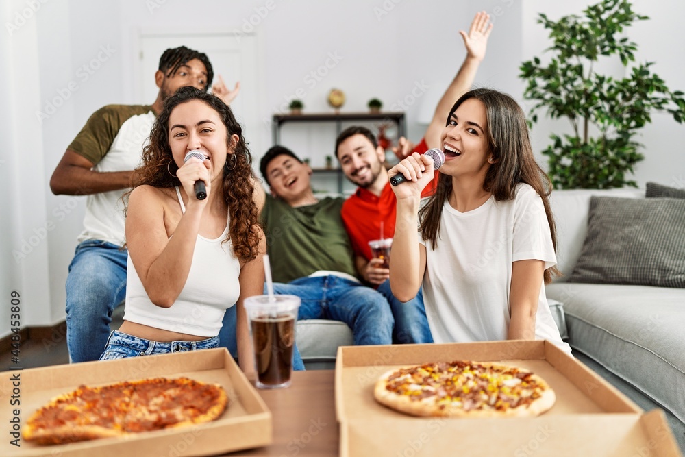 Group of young friends having party eating italian pizza and singing song at home.