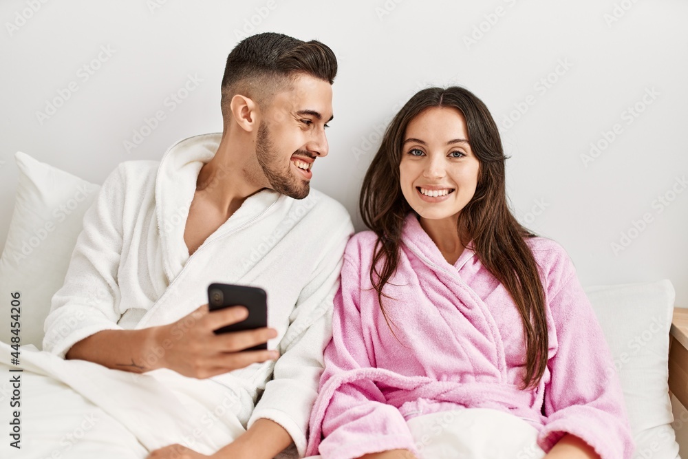 Young hispanic couple using smartphone lying on bed at home. Young hispanic couple using smartphone lying on bed at home.