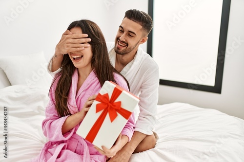 Young hispanic couple smiling happy surprising with gift at bedroom.