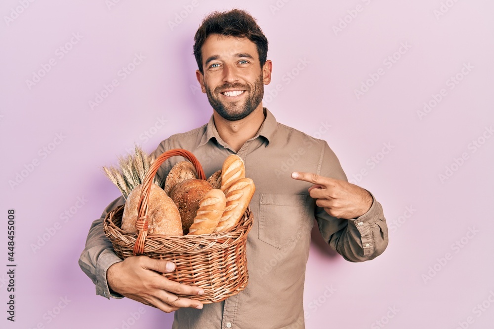Handsome man with beard holding wicker basket with bread smiling happy pointing with hand and finger Handsome man with beard holding wicker basket with bread smiling happy pointing with hand and finger
