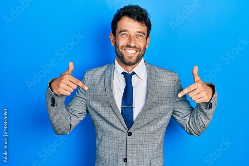 Handsome man with beard wearing business suit and tie looking confident with smile on face, pointing oneself with fingers proud and happy.