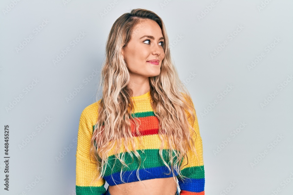 Beautiful young blonde woman wearing colored sweater smiling looking to the side and staring away thinking. Beautiful young blonde woman wearing colored sweater smiling looking to the side and staring away thinking.