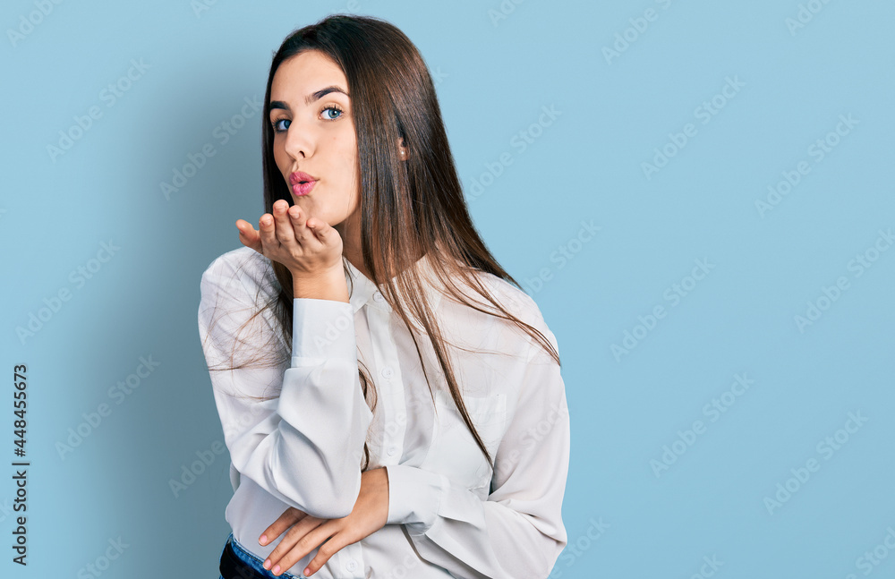 Young brunette teenager wearing business white shirt looking at the camera blowing a kiss with hand on air being lovely and sexy. love expression. Young brunette teenager wearing business white shirt looking at the camera blowing a kiss with hand on air being lovely and sexy. love expression.