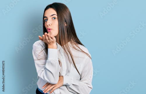 Young brunette teenager wearing business white shirt looking at the camera blowing a kiss with hand on air being lovely and sexy. love expression.