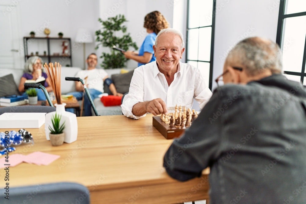 Two retired man smiling happy playing chess at nurse home. Two retired man smiling happy playing chess at nurse home.