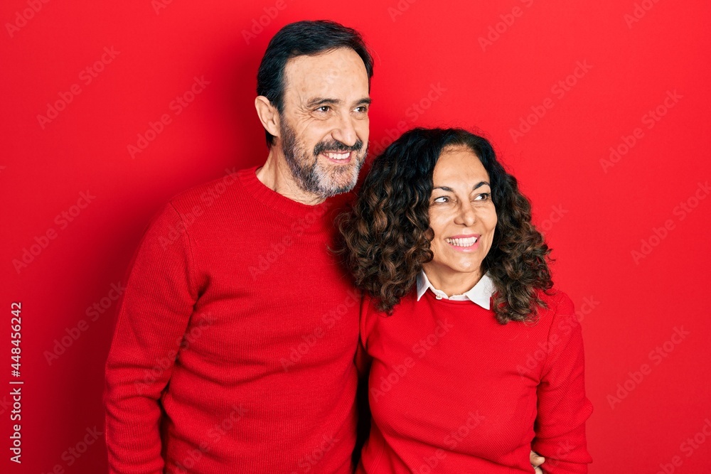 Middle age couple of hispanic woman and man hugging and standing together looking away to side with smile on face, natural expression. laughing confident. Middle age couple of hispanic woman and man hugging and standing together looking away to side with smile on face, natural expression. laughing confident.