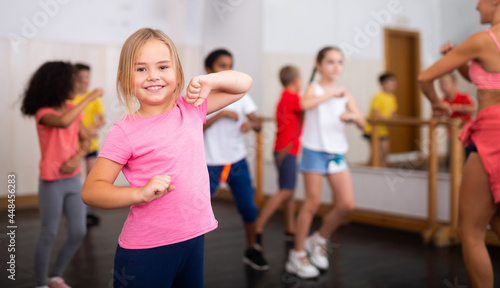 Smiling little girl training movements of vigorous dance with group of tweens in children dance studio © JackF